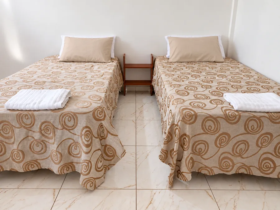 Habitación con dos camas individuales de ropa de cama beige, toallas blancas y mesita de luz central